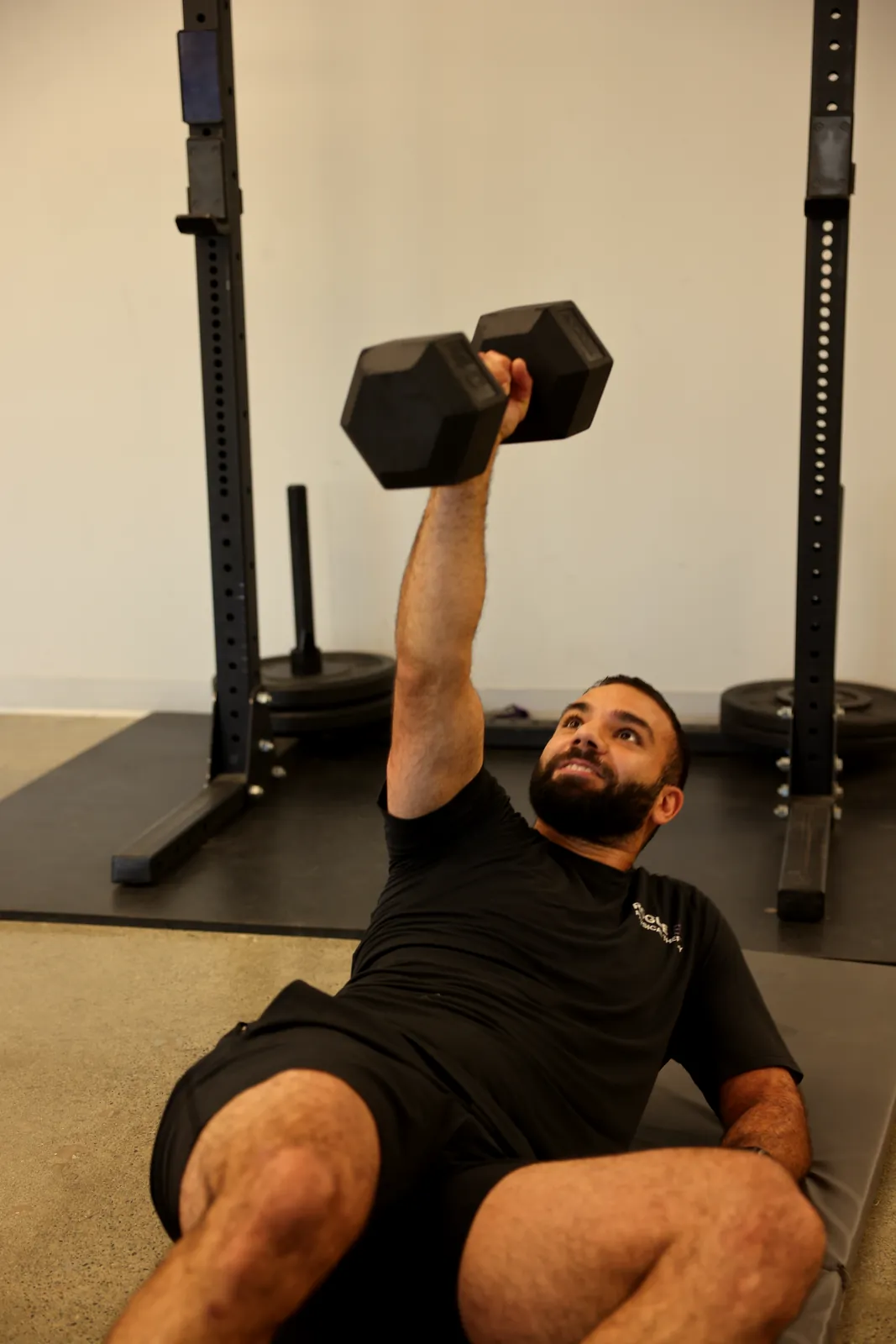 Person doing a floor-based dumbbell press exercise by a squat rack.